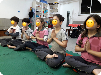 Crianças sentadas lado a lado em postura de prece, praticando concentração no yoga