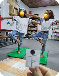 Crianças praticando postura da árvore em equilíbrio sobre tatames, durante aula lúdica de yoga