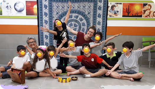 Turma reunida ao fim da aula de yoga, com tapete azul e brinquedos educativos no centro
